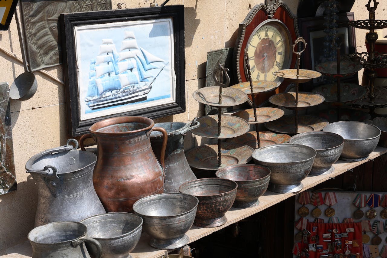 Antique shop display featuring vintage metalware, a ship painting, and a clock.