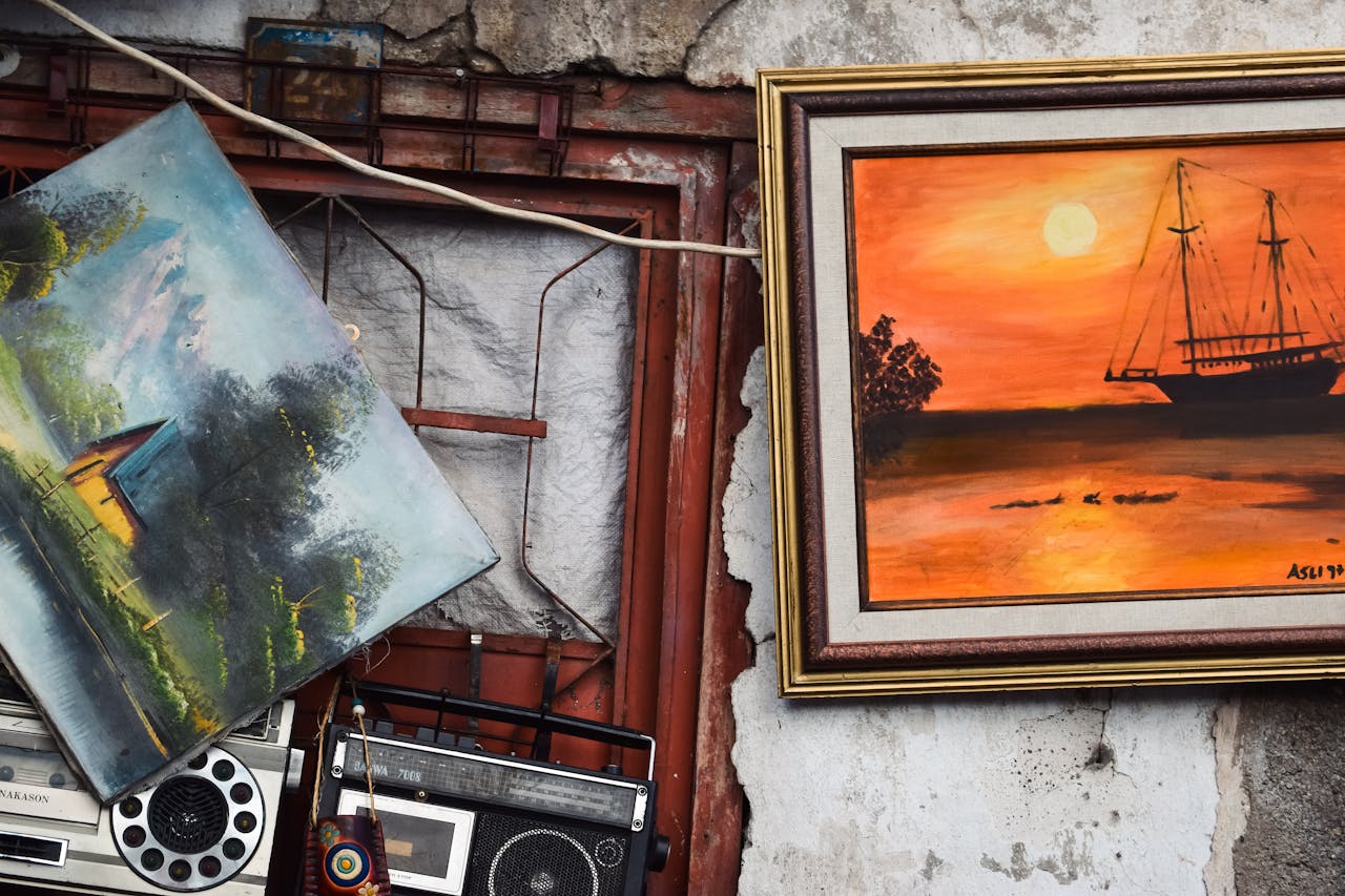 about-01 A collection of vintage paintings and radios mounted on a rustic wall, showcasing artistic and antique charm.